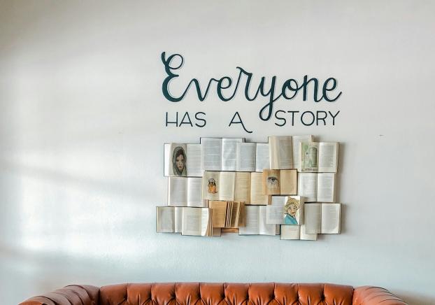 Everyone has a story above a brown leather couch in front of a white wall